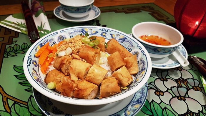 54a Bun Reisnudeln, gewürzt mit verfeinerter Süß-sauer-Fisch-Sauce, serviert in einer grossen Schale mit Thai-Basilikum, Eisbergsalat, Gurken, eingelegtem Karottensalat, Erdnüssen und vegetarischen Frühlingsrollen (Gemüse- und Tofufüllung)